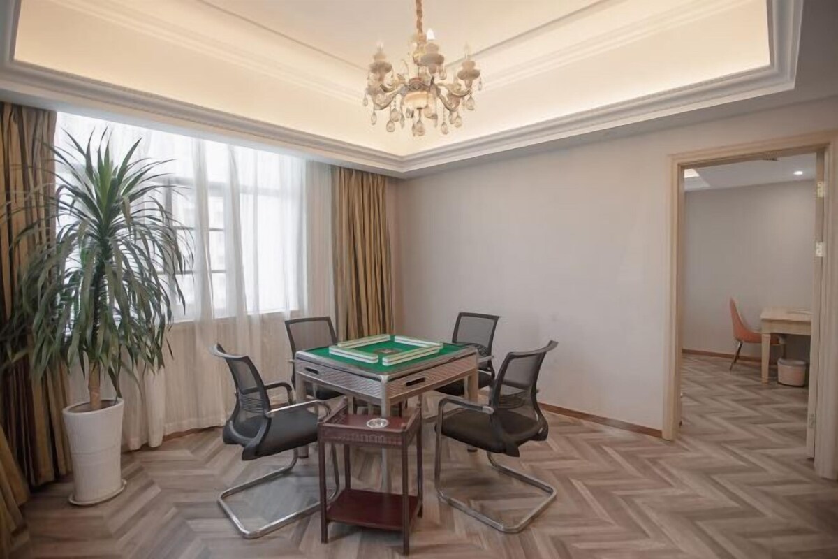 A room with a green pool table, four chairs, a chandelier, a potted plant, and a window with curtains.