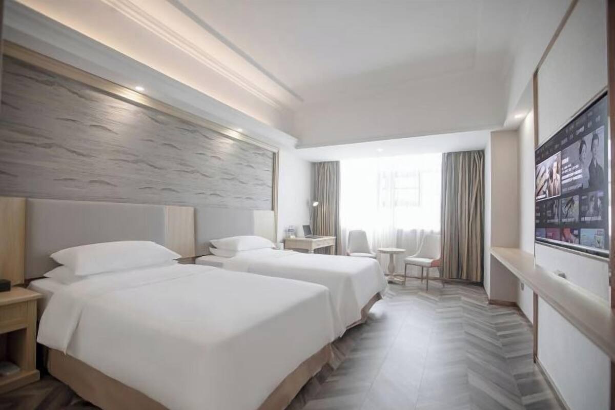 A hotel room with two beds, a desk, a chair, a TV, and a large window.