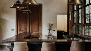 A bar area with a dark countertop, three stools, hanging pendant lights, and a wooden door in the background. - Private Pool • Riverside Yoga Shala • Ubud (Ubud)
