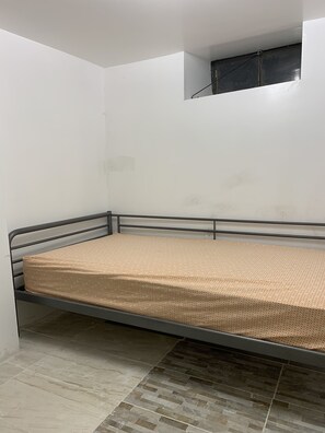 A single bed with a metal frame in a room with white walls and a tiled floor.