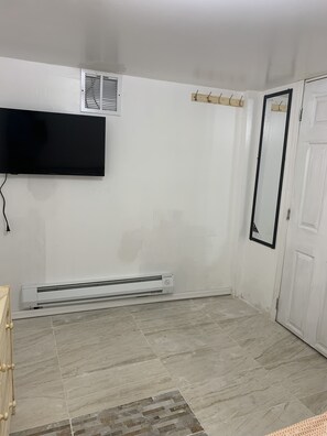 A room with a flat-screen TV mounted on the wall, a white door, and a white radiator on the floor.