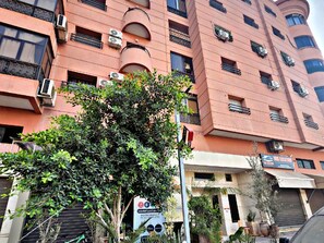 Un immeuble à plusieurs étages doté de balcons, de climatiseurs et d’une enseigne indiquant qu’il s’agit d’un établissement proposant des services de localisation.
