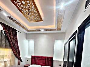 Une chambre d’hôtel moderne avec une tête de lit rouge, un plafond décoratif et une grande fenêtre avec des rideaux.