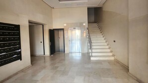 Un couloir doté d’un sol en marbre, d’un escalier et d’une rangée de casiers numérotés sur le côté gauche.