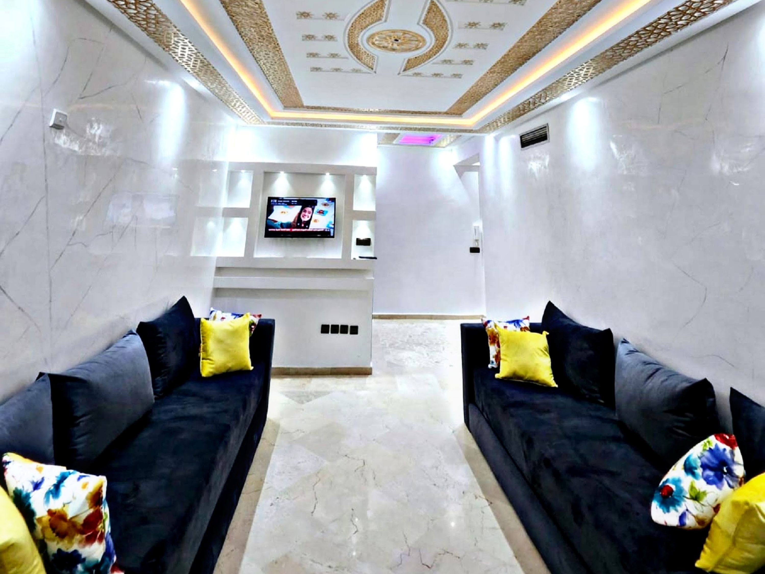 A modern living room with two dark sofas, a flat-screen TV mounted on the wall, and a patterned rug on the floor.