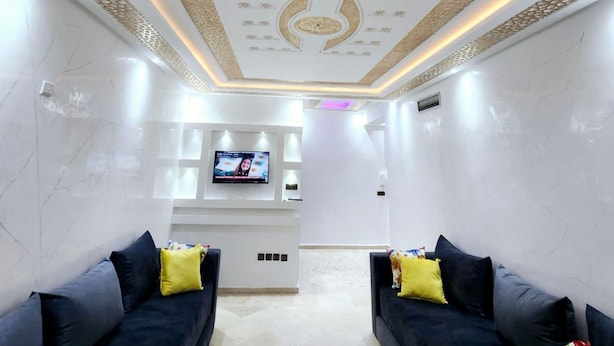 Une pièce moderne avec deux canapés sombres, un téléviseur à écran plat fixé au mur et un plafond décoratif.