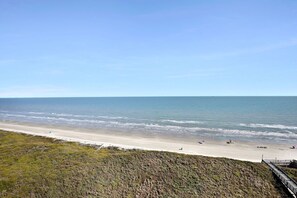 Una playa con arena, una zona verde al frente y un cielo azul despejado.