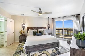 Un dormitorio con una cama grande, ventilador de techo, lámparas de noche, vistas al océano y un balcón con barandilla.