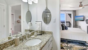 Une salle de bain moderne avec un comptoir en granit, un grand miroir et un ventilateur de plafond.