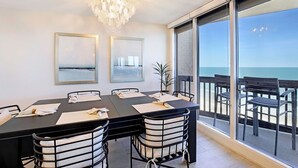 Un coin repas avec une table noire, des chaises blanches et un lustre. Deux tableaux encadrés ornent le mur, et une plante en pot est posée sur la table.