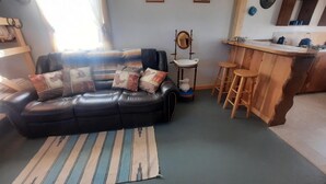 Una sala de estar con un sofá de cuero negro, un tapete a rayas y una zona de bar con taburetes de madera.