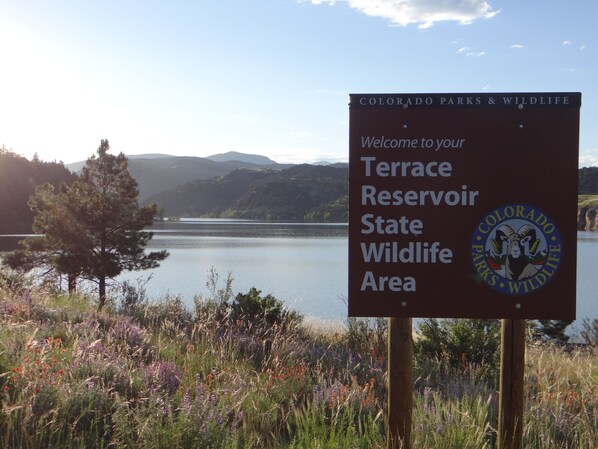 A sign welcoming visitors to the Terrace Reservoir State Wildlife Area, featuring a scenic view of a lake and mountains.