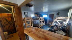 Interior rústico de una cabaña con barra de madera, literas y una pequeña zona de estar.