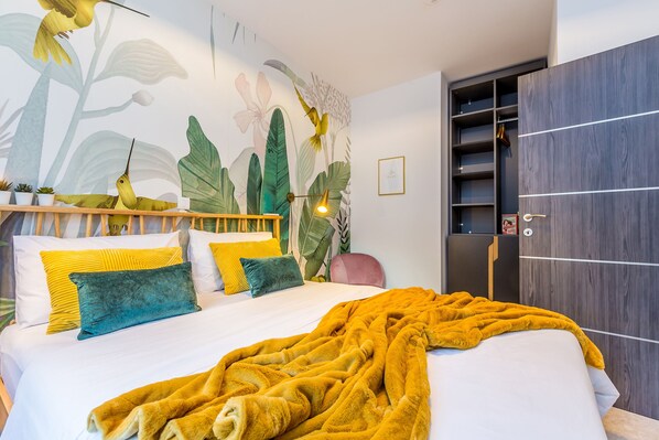 A bedroom with a bed, a yellow blanket, and a wall mural of birds and plants.