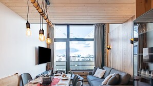 A modern dining area with a wooden table set for a meal, a sofa, and a large window offering a mountain view.