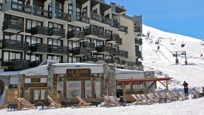 A multi-story hotel with balconies, a bar/restaurant, and ski lift chairs on a snowy slope.