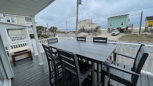 A covered outdoor deck with a table and chairs, overlooking a beach with houses and a truck. - FENCED IN 2nd Row 2 the sea❤️ Shibumi, beach chairs, and linens included. (Surf City)