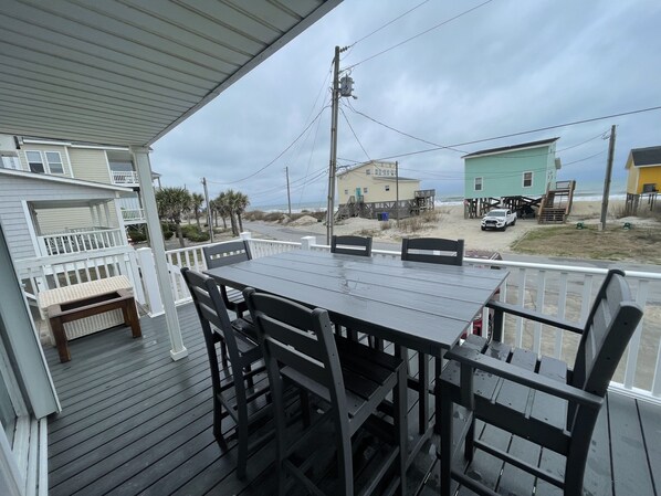 A covered outdoor deck with a table and chairs, overlooking a beach with houses and a truck. - FENCED IN 2nd Row 2 the sea❤️ Shibumi, beach chairs, and linens included. (Surf City)