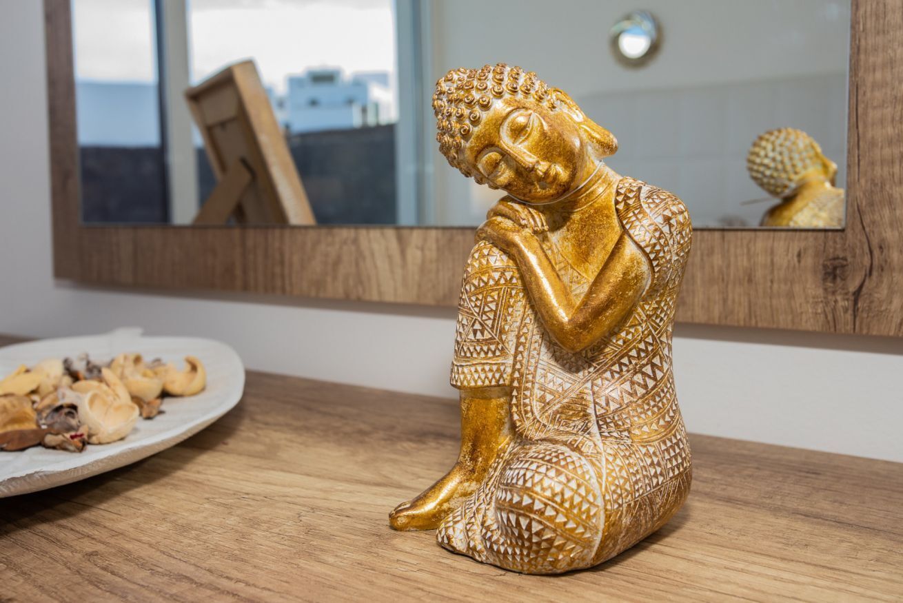 Eine goldene Buddha-Statue steht auf einem Holztisch, daneben ein Teller mit Keksen.