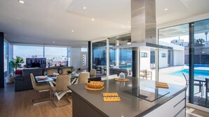Une cuisine moderne dotée d’un îlot central, de grandes fenêtres et d’une vue sur une piscine.