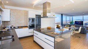 Une cuisine moderne dotée d’un îlot central, d’un four encastré et d’une grande fenêtre offrant une vue sur la ville.