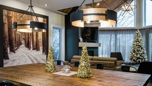 Ein modernes Wohnzimmer mit einem großen Esstisch aus Holz, zwei Weihnachtsbäumen und einem Kamin.