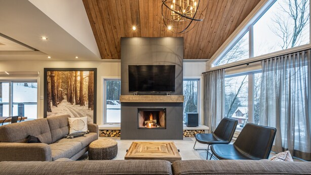 Ein modernes Wohnzimmer mit Kamin, großem Fernseher und Blick auf eine verschneite Landschaft durch große Fenster.