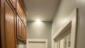 A narrow hallway with wooden cabinets and a microwave on the left, a white door at the end, and a white door with glass panels on the right. - Stylish 1 bedroom studio with kitchenette (Jackson)