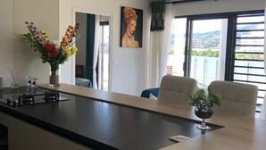 Eine moderne Küche mit Kochinsel, einem Essbereich mit zwei Stühlen, einem Gemälde an der Wand und Blick auf die Stadt durch große Fenster.