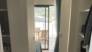 Ein Flur, der zu einem Balkon mit Tisch und Stühlen führt, ein Bett mit einem gemusterten Überwurf und eine Aussicht auf eine Hügelkuppe.