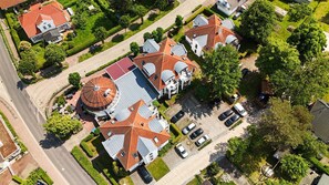 Oversigtsbillede af et boligområde med flere huse, en central bygning med et karakteristisk tag og et parkeringsområde.