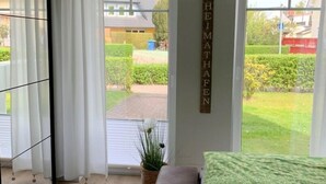 Une chambre à coucher avec un lit, un canapé, une fenêtre avec des rideaux, une plante en pot et un panneau accroché au mur.