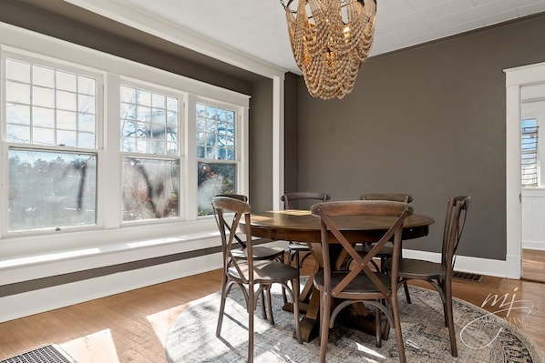 Un coin repas avec une table ronde, six chaises en bois et un lustre.
