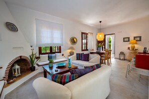 Una sala de estar acogedora con chimenea, sofás blancos, un comedor y un ambiente luminoso y agradable.