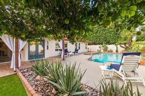 A backyard with a swimming pool, a covered patio, and a fruit tree.