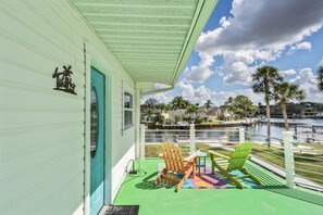 A balcony with a view of a waterfront, featuring a green deck, two Adirondack chairs, and a small table. - Cotee River Tiki Hut (New Port Richey)