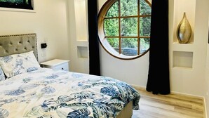 Une chambre avec un grand lit, une fenêtre ronde et une vue sur la verdure.