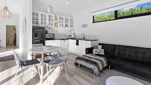 Une cuisine moderne avec des meubles blancs, un réfrigérateur noir et un coin repas comprenant une table ronde et des chaises.
