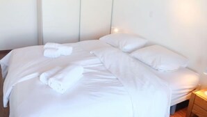 Un lit bien fait, avec du linge de lit blanc et des oreillers, une table de chevet avec une lampe et une armoire avec un miroir.