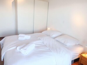 A neatly made bed with white linens and pillows, a bedside table with a lamp, and a wardrobe with a mirror.