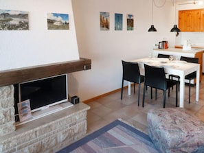 A living room with a stone fireplace, a TV, and a dining area with a table and chairs.