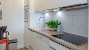 A modern kitchen with white cabinets, a stainless steel sink, a built-in oven, and a black induction cooktop.