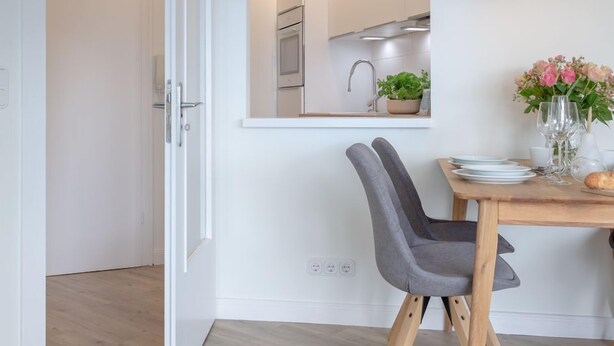 A modern dining area with a wooden table, grey upholstered chairs, and a hanging pendant light.