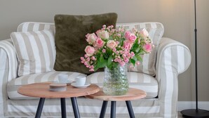 A living room with a striped sofa, a glass vase with flowers, a round wooden table, and a floor lamp.