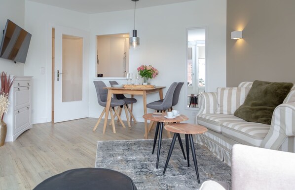 Un salon moderne comprenant un canapé, une table à manger avec des chaises, un téléviseur fixé au mur et une petite table d’appoint.