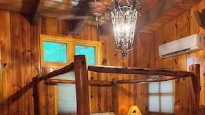 A wooden four-poster bed with a plaid bedspread and pillows, a hanging wrought iron chandelier, and a window with a view of the forest. - Big Sam Hangout!! 4 bed 3.5 bath South End with rear privacy & Hot Tub (Brookeland)