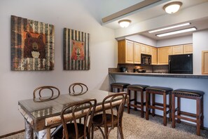 Eine moderne Küche mit Holzausstattung, einem schwarzen Kühlschrank und einem Glastisch mit vier Stühlen.