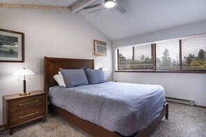 Ein Schlafzimmer mit Bett, Nachttisch, Lampe und einem Fenster mit Jalousien.