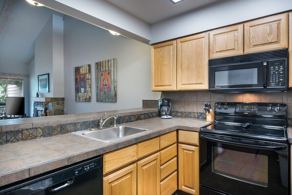 A modern kitchen with wooden cabinets, a black microwave, a stove, and a dishwasher. - Waterfront condo w/fireplace, balcony & incredible views - Marina Cay Landing (Bigfork)