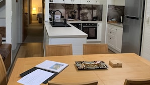 A modern kitchen with white cabinets, a stainless steel refrigerator, and a dining area with a wooden table and chairs. - TreeTops - wood fire, outdoor spa and great coffee (Hepburn Springs)